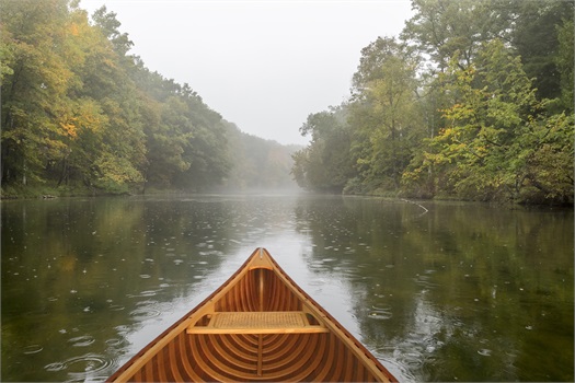 front of canoe on lake surrounded by trees